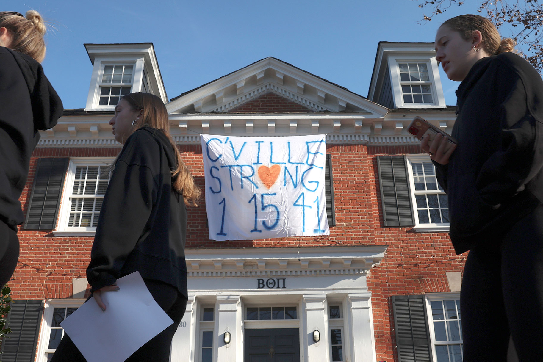 Students walk past a fraternity house with a banner memorializing three University of Virginia football players