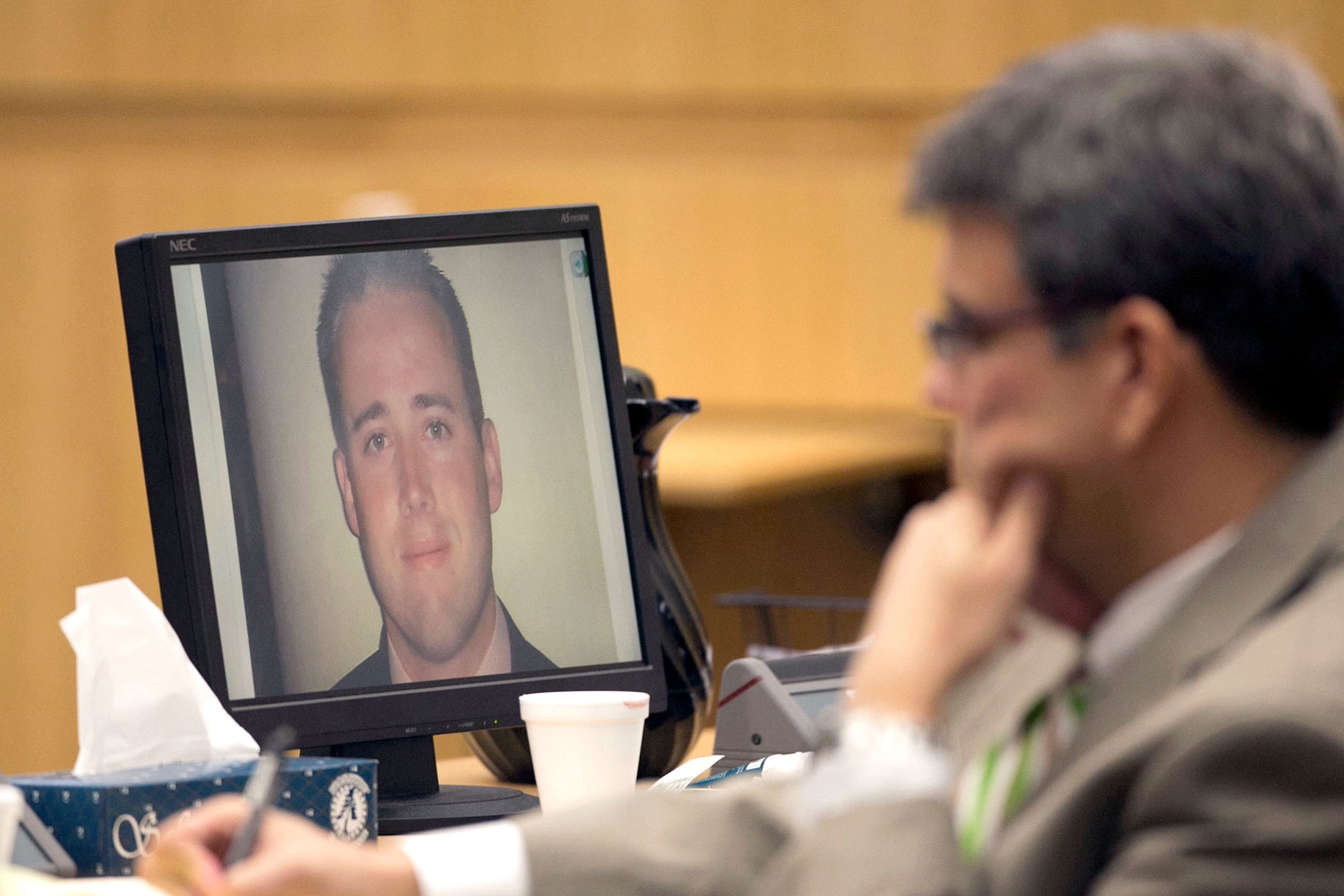 A photograph of Travis Alexander appears on a computer monitor