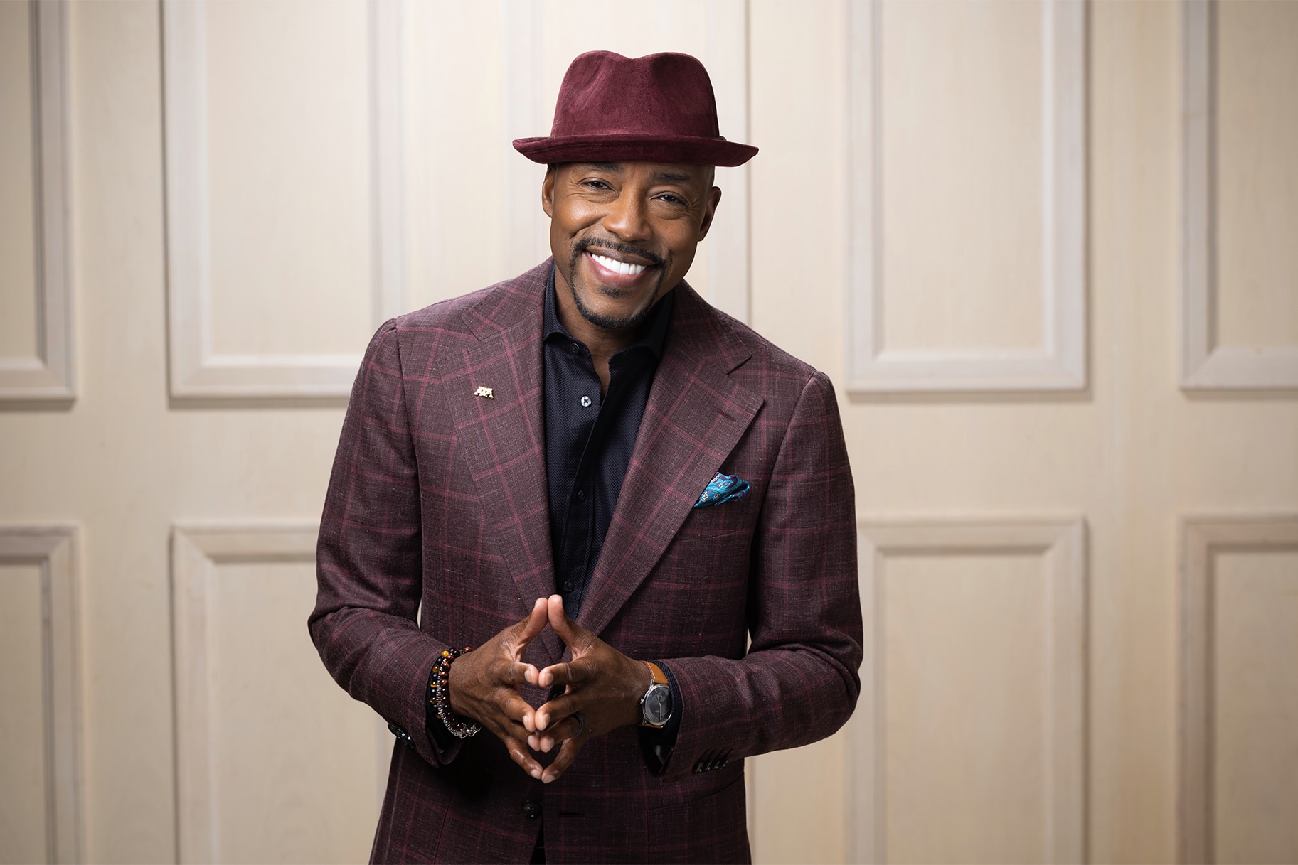A headshot of Will Packer wearing a purple had and suit