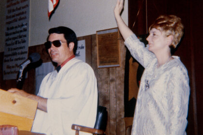 Jim Jones and his wife, Marceline preaching standing at a podium