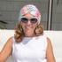 Debrah Lee Charatan wearing a white dress and head scarf and sunglasses sits on a lounge chair smiling