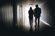 A Business Woman and Business Man walk down a dark hallway together