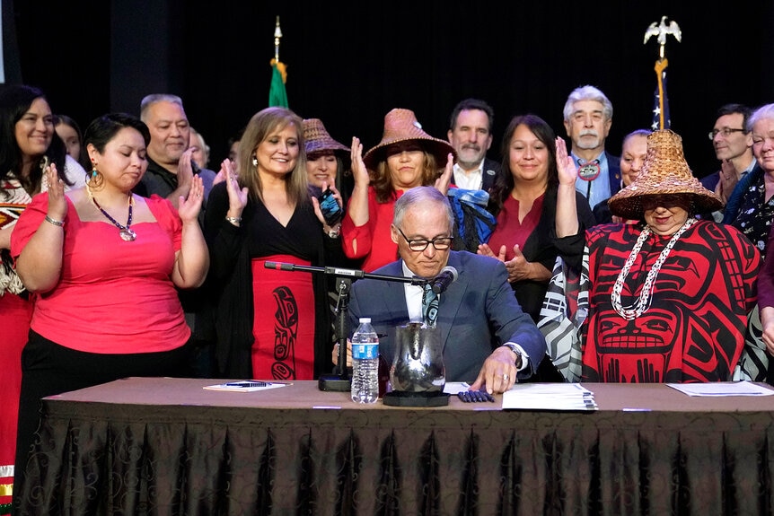 ay Inslee, center, reaches for a pen as tribal leaders and other supporters applaud after he signed a bill