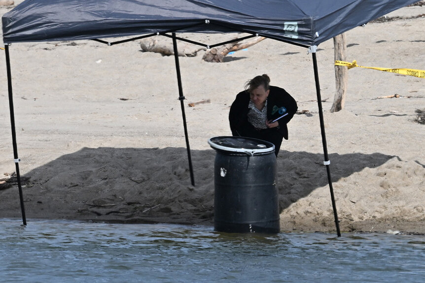 An official stands next to a barrel where a body was discovered in Malibu Lagoon State Beach, CA.