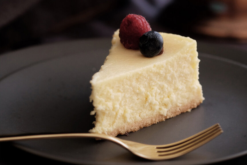 A cheesecake with berries on a grey plate with a gold fork.