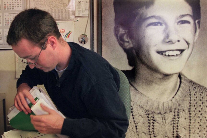 Dennis Whipple looks through papers with a photo of Jacob Wetterling behind him