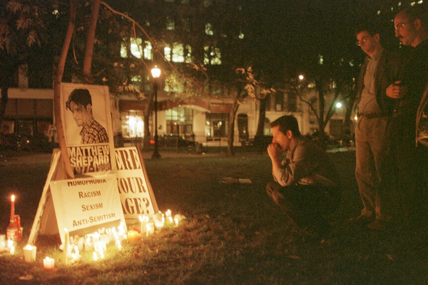 A person squats in front of a candlelight vigil for Mathew Shepard